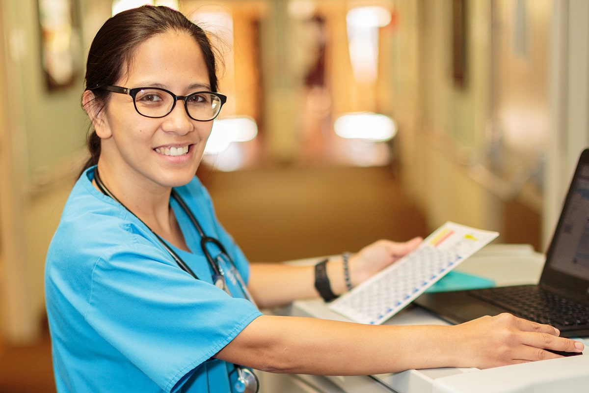 Nurse sitting in front of a laptop and smiling